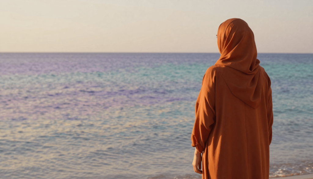 Muslim revert woman in a rust abaya standing by the sea, symbolising trauma healing and inner calm for Muslim women